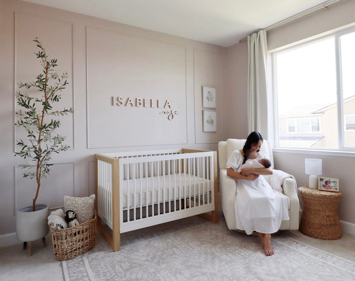 A baby's nursery with a white crib, pink walls, a white chair and a nursery name sign