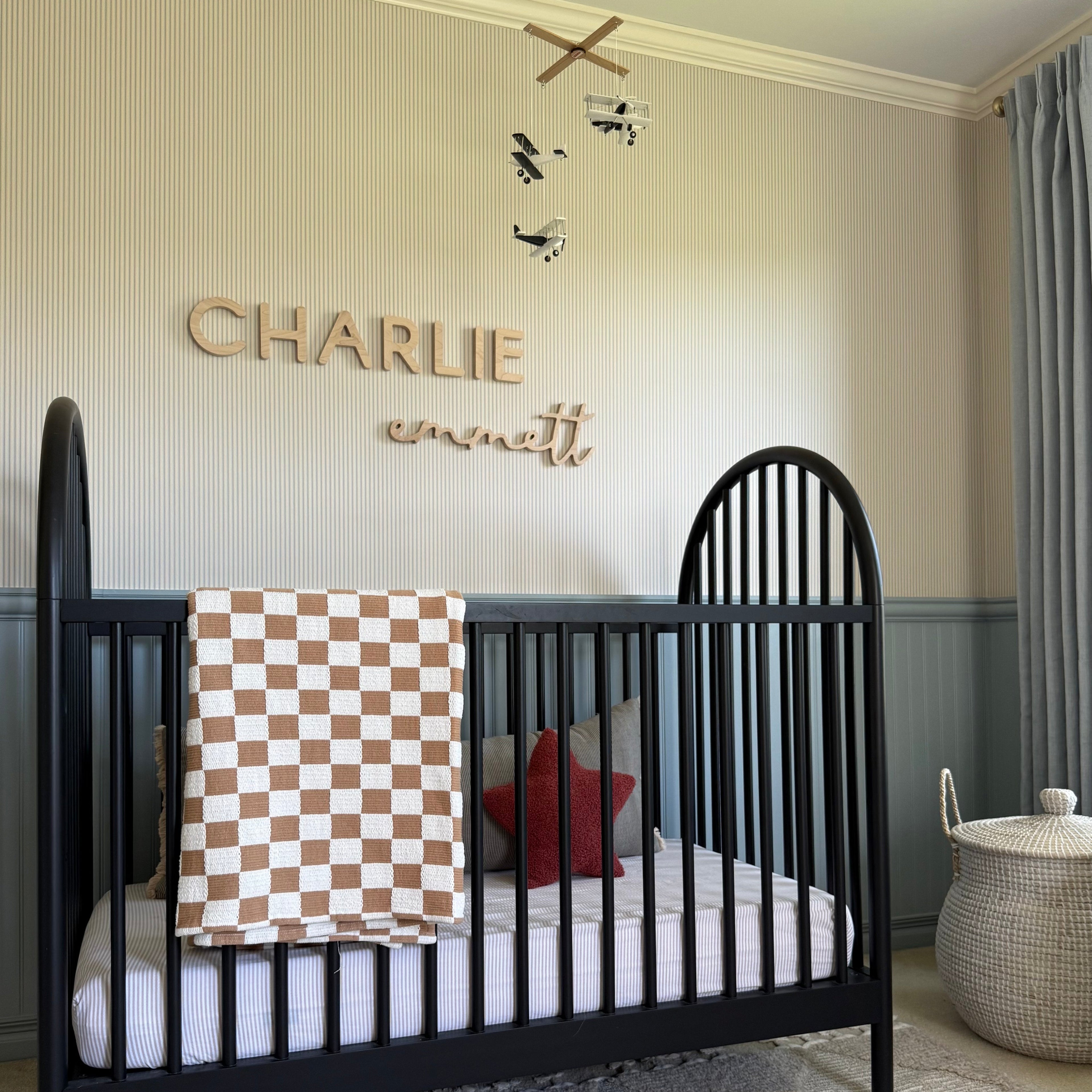 Nursery room with a black crib, checkered blanket, and decorative wall name 'CHARLIE'.