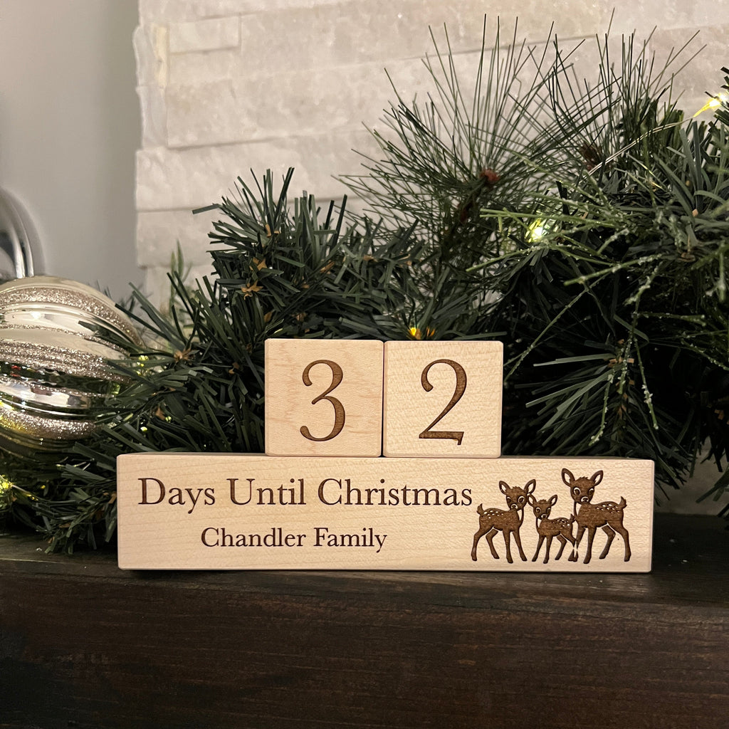 Wooden Christmas countdown blocks with reindeer design next to a decorated Christmas tree.