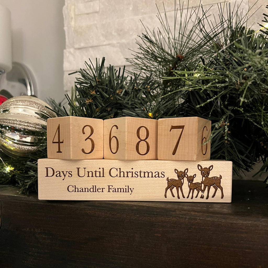 Wooden blocks counting down to Christmas with a reindeer design, placed against a Christmas tree.