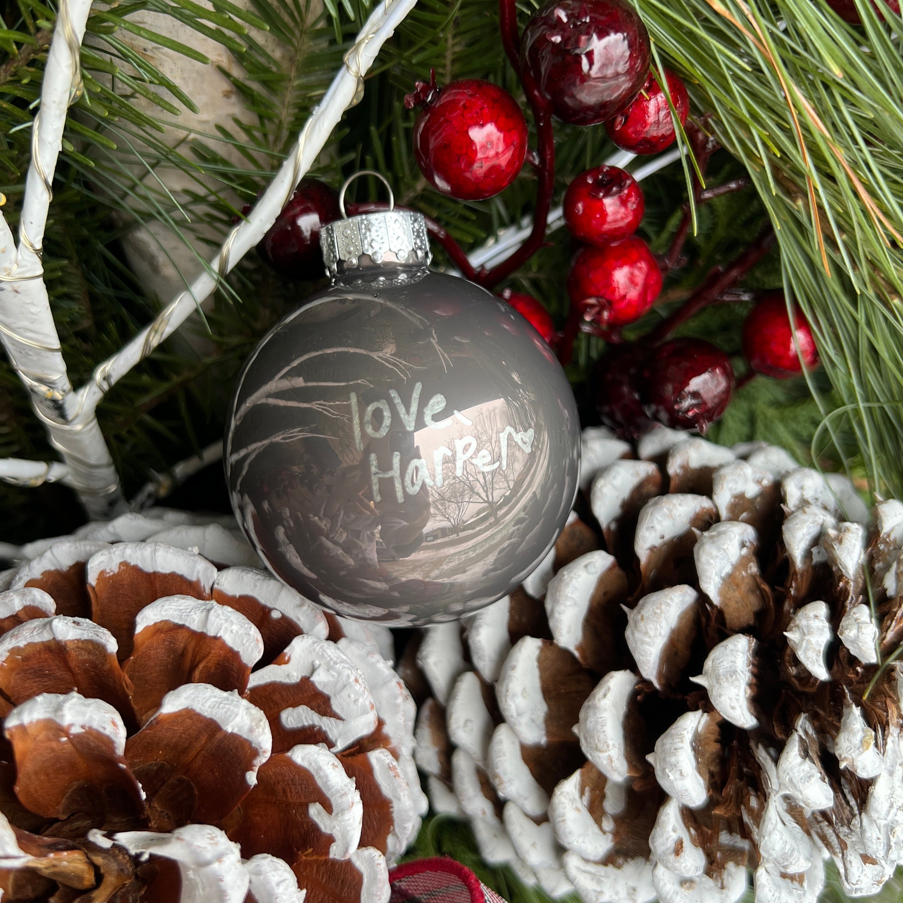 Decorative Christmas ornament with engraved text on a branch with pinecones and berries.