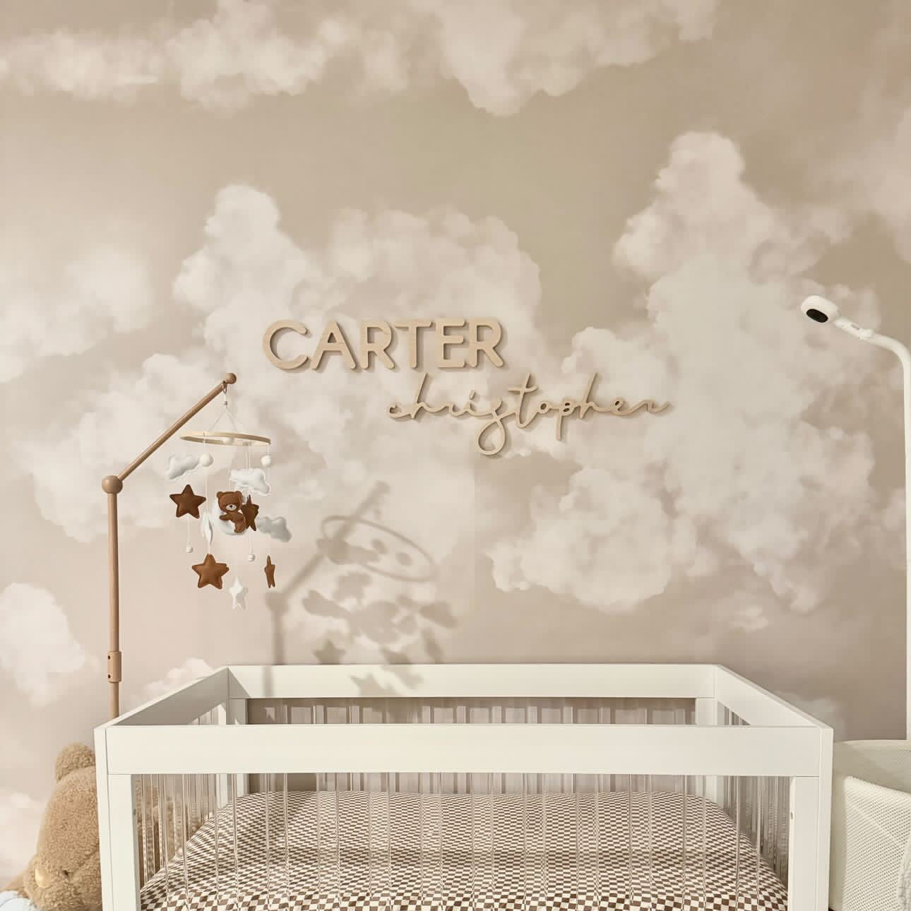 cloud wallpaper with wooden name sign above crib