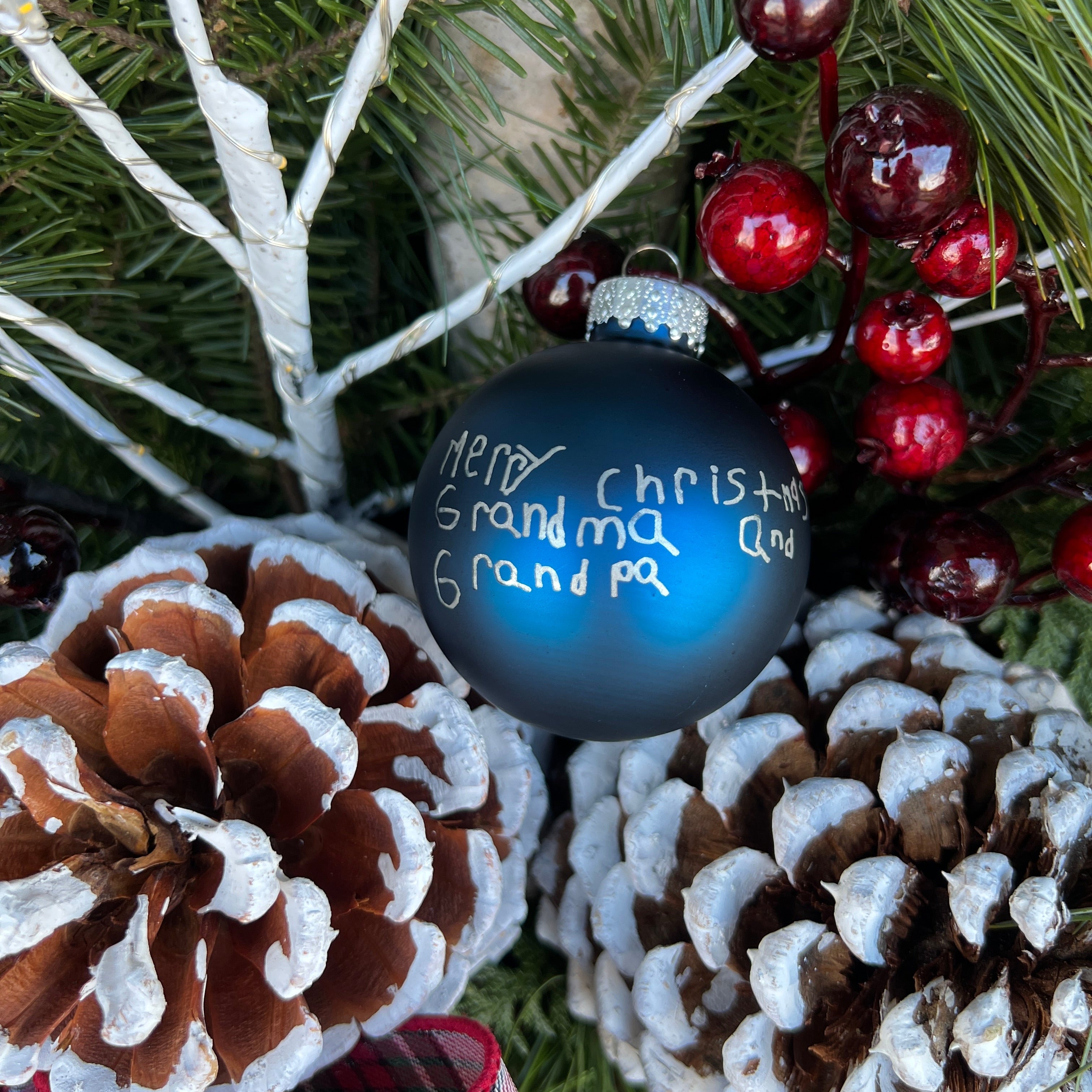 Decorative Christmas ornament with 'Merry Christmas to Grandma and Grandpa' text, surrounded by pine cones and berries.