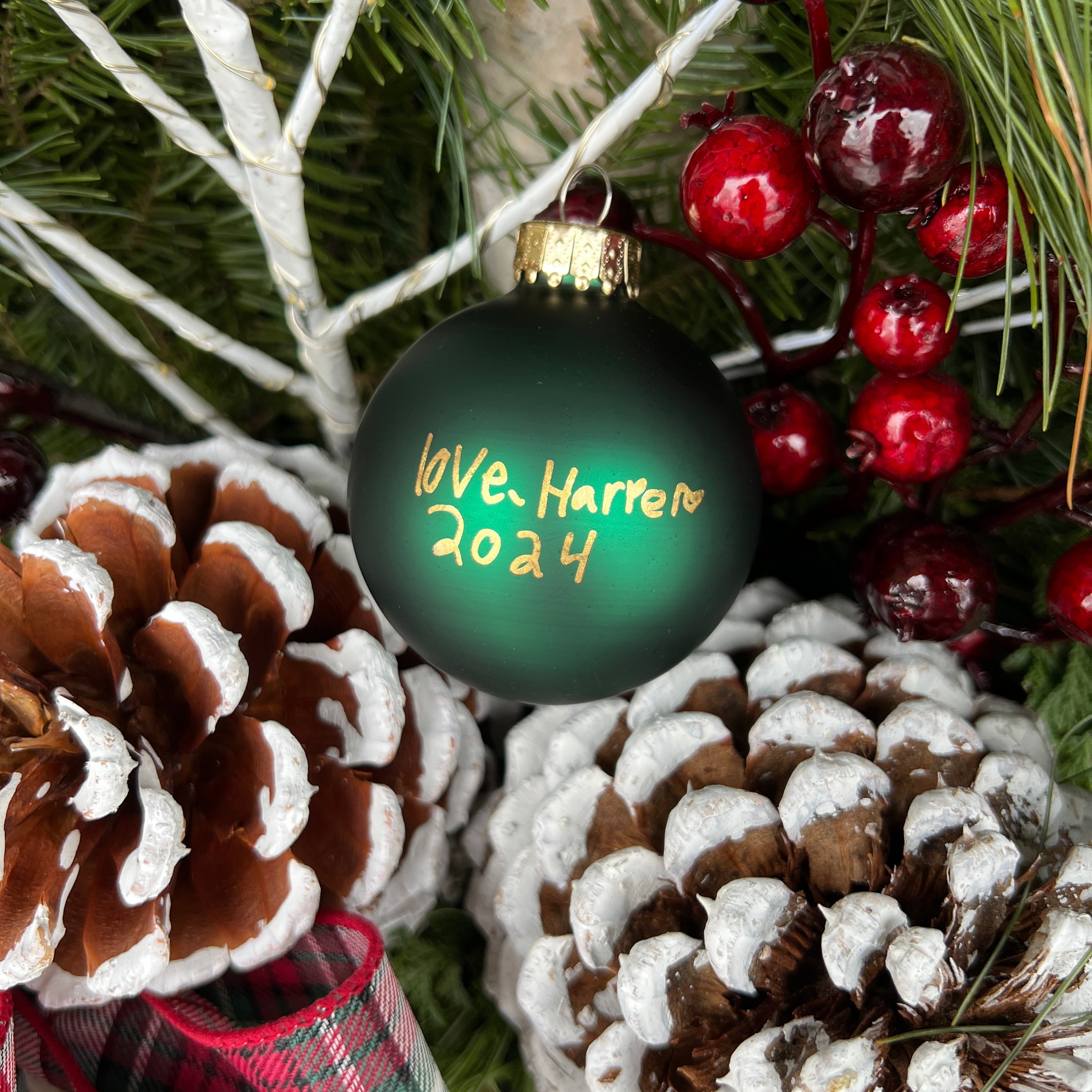Decorative Christmas ornament with 'Love. Harlen 2024' text, surrounded by pine cones and berries.