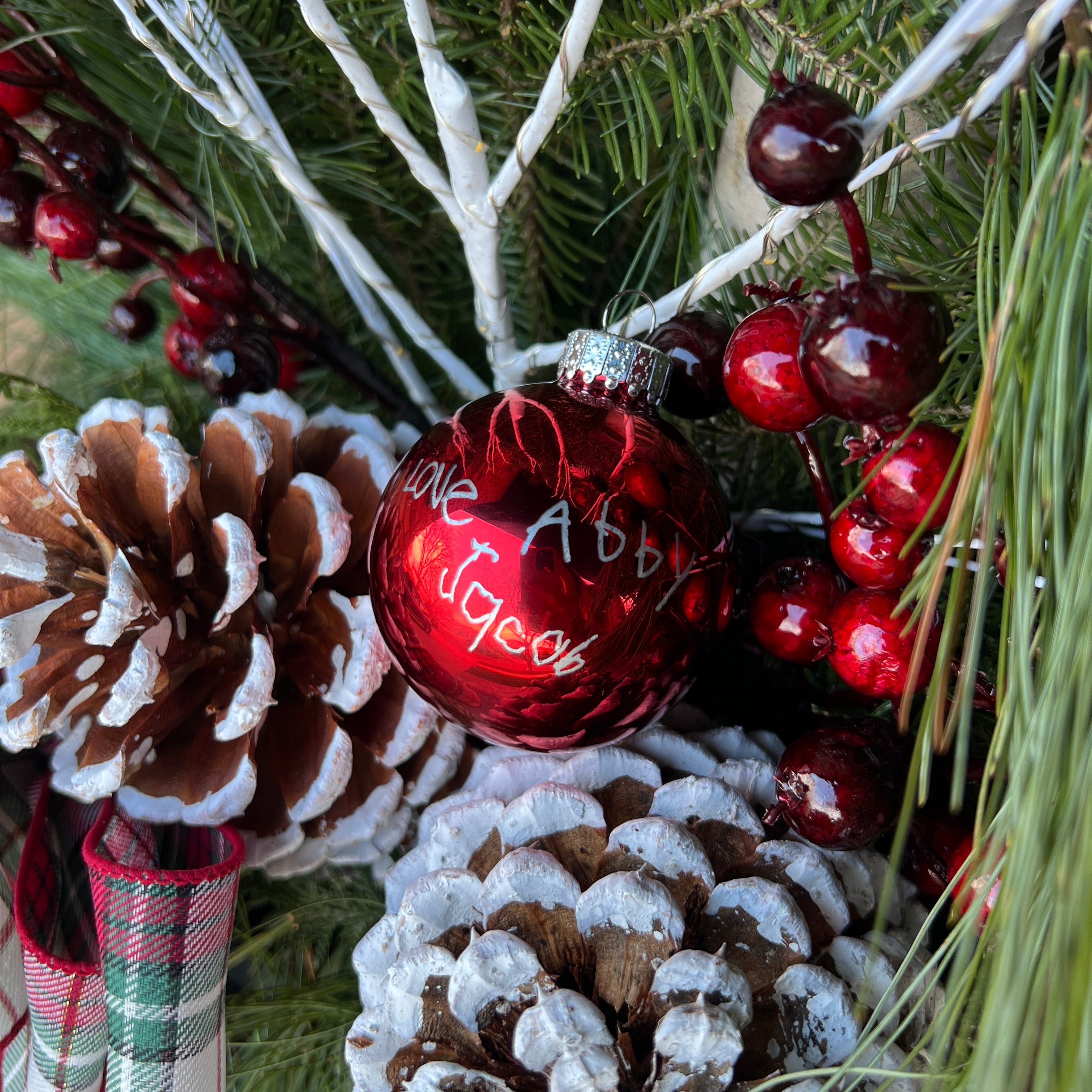 Decorative Christmas arrangement with red ornament, pine cones, and berries.